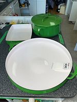 All three pieces (wok-shaped pan, rectangular pan, Dutch oven with lid) arranged on countertop