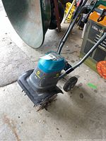 Full side view of the Yardworks electric tiller showing the handlebars, body, wheels, and tilling blades on the concrete floor.