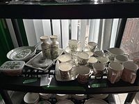 Multiple porcelain Market pattern items arranged on black shelving: mugs, cups, saucers, serving pieces, and vases