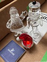 Overview showing one Santa figurine, one nutcracker figurine, red Santa hat ornament and Swarovski certification booklet