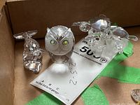 Box containing clear crystal owl, dolphin and sea turtle figurines on a note with measurements