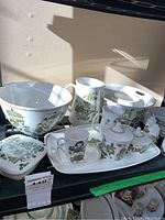 Overview of assorted bowls, pitchers, tureen, lidded dishes, candle holders, plates, platter, salt and pepper shakers on shelf