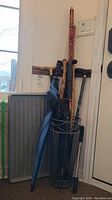 Photo showing the metal umbrella stand holding multiple canes, umbrellas, and the resin boot mat leaning beside it.