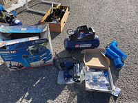 Full kit overview: compressor, boxed accessories, brad nailer and coiled hose on pavement