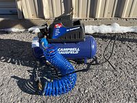 Side/front overview showing compressor tank, motor housing, coiled hose and blow gun on asphalt