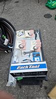 Wide view showing bike tools and Park Tool parts organizer with multiple boxed items in original packaging, some loose tools visible.