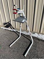 Full side view of the Blackburn bike work stand showing the white metal frame, triple leg base, red jaws, and metal accessory tray.