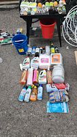 View of all assorted bicycle maintenance bottles, aerosols, and containers arranged on the ground and tables including buckets.