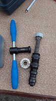 Puller handle tool with blue grips, insert tool with spring, metal grooved ring laid on tan fabric surface