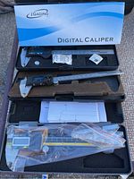 Three digital calipers with cases shown from above, one is iGAGING brand in blue and black case, others are black digital calipers in foam-lined cases.