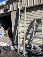 Full view of the aluminum extension ladder standing upright against a roller door, showing the two sections and the rubber caps at the top.