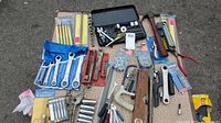Wide view of the assortment of hand tools including wrenches, sockets, hammer, hex keys, taps, and more placed on a textured surface.