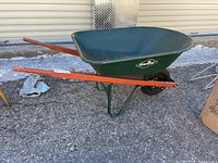 Side view of green Garant heavy duty wheelbarrow with wooden handles and metal bucket.