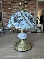 Front view of one etched glass and brass touch table lamp showing floral design on glass shade and brass base with ceramic flower accent.