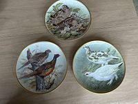 Three decorative plates featuring illustrations of game birds by Basil Ede arranged together on a table.
