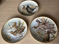 Three decorative plates depicting gamebirds, each about 9 inches diameter with detailed bird paintings by Basil Ede.