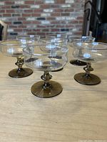 Seven smoky brown stemmed compote glasses shown together on a wooden surface, clear bowl with smoky brown pedestal base.