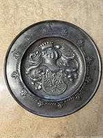 Close-up of one vintage pewter plate showing crowned helmet and heraldic crest.