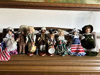 Wide shot of all 8 vintage Revolutionary War era dolls lined up together on a wooden surface, showing detailed period costumes including 2 Betsy Ross dolls and other soldiers and civilians.