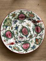 Close-up photo of a porcelain plate with colorful floral and botanical patterns including pink flowers and green leaves.