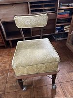 Full view of vintage sewing chair with marigold vinyl padded seat and backrest on casters.
