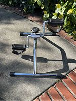 Side angle showing one pedal and overall design, chrome frame with two legs touching the ground and one extended leg.