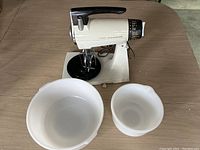 Sunbeam Mixmaster stand mixer on base with large and small white mixing bowls on a wooden table