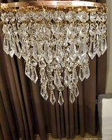 Close up of gold color chandelier with clear crystal prisms hanging in multiple tiers in an elaborate design.