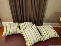 Photo of four outdoor cushions with striped green and beige pattern arranged on a wooden surface.