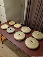 Eight weight plates on table: four large approx. 10lb and four smaller approx. 5lb plates in beige/tan color, plastic coated with wear on one plate.
