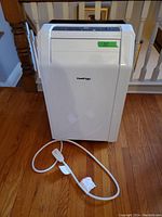White KoolKing portable air conditioner with power cord on wooden floor.