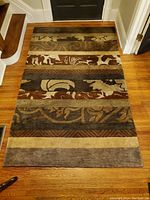 Full view of the rectangular area rug placed on hardwood floor showing multi-band color pattern in earth tones with abstract and foliage motifs.