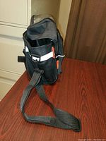 Side view of black heavy fabric bicycle handlebar bag featuring a long adjustable strap, mesh pocket, and reflective strip.
