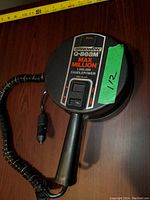 Front view of handheld spotlight with label showing brand and model, coiled power cord, and cigarette lighter plug.