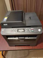 Top-front view of the Brother DCP-7065DN printer on a desk showing the paper output slot, control panel, and document feeder.