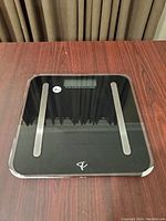 Top view of black digital bathroom scale, showing glass surface, LCD display, and sensor strips.