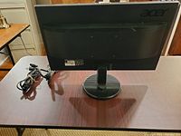 Back view of a black Acer computer monitor showing the logo, stand, and included cords coiled at the side.