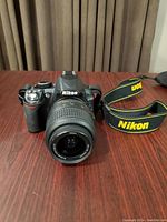 Nikon D3100 body with 18-55mm kit lens attached and Nikon strap on table