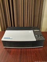 View of Oreck XL air cleaner on wooden table. The air cleaner is rectangular with a silver and black color scheme. Top right control panel visible.