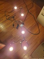 View of four illuminated puck lights on black cable laid on wooden floor, showing spacing and light quality.