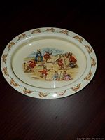 Top down view of oval Royal Doulton Bunnykins dish showing central design of rabbits and decorative rabbit border along rim.