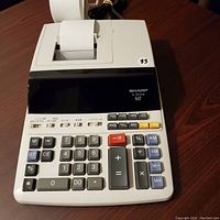 Front view of Sharp EL-2155PI office calculator with built-in printer and paper roll visible.