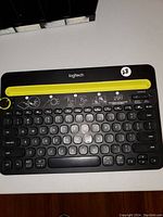 Top view of Logitech K480 wireless keyboard showing black keys and yellow cradle with control knob
