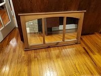 Front view of the maple finish wood framed mirror leaning against dark wood furniture on a hardwood floor.