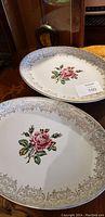 Photo showing two oval porcelain dishes with pink rose floral motif and gold gilded ornate edges placed on wooden table.