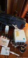 Photo shows Luminess Air brush compressor unit, airbrush gun, multiple small bottles of makeup or paint liquids, cleaning solution, and black carrying case on wooden surface.