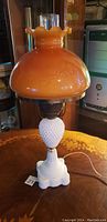 Full view of antique amber milk glass lamp showing white hobnail milk glass base and amber ruffled shade.