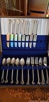 Full view of antique hand hammered cutlery set in a box with knives, forks, spoons, and cutting tool.