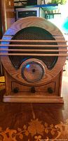 Front view showing wooden cabinet, three control knobs, and circular dial tuner with black speaker grille.