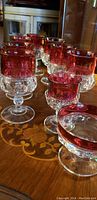 Nine ruby red overlay crystal goblets arranged on a wood table, front glass in focus